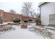 Snowy backyard featuring a brick fire pit, fence, and partial view of the home's exterior at 12107 E Vassar Dr, Aurora, CO 80014