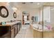 Well-lit bathroom featuring dual sinks, a soaking tub, tiled floors, and a view to the main bedroom at 282 Vialpando St, Brighton, CO 80601