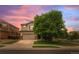 Charming two-story home with a manicured lawn, mature tree, and attached two-car garage at sunset at 10197 Quintero St, Commerce City, CO 80022