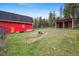 Exterior of property showing a large red barn, a storage outbuilding, and ample green lawn and treed backdrop at 31551 Black Widow Dr, Conifer, CO 80433