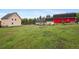 Wide view of the property showing large grassy area, multiple buildings, treed backdrop, and fencing at 31551 Black Widow Dr, Conifer, CO 80433