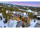 Stunning aerial view of a luxurious mountain home surrounded by snow-covered slopes and trees at dusk at 422 Timber Trail Rd, Breckenridge, CO 80424
