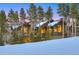 Picturesque log home with large windows, nestled among mature pine trees and snow-covered ski hill at 422 Timber Trail Rd, Breckenridge, CO 80424