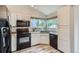 Well-lit kitchen featuring white cabinets, black appliances, and a large window overlooking the backyard at 11481 King St, Westminster, CO 80031