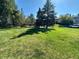 A well-manicured front lawn features mature trees casting shadows and a glimpse of nearby homes on a sunny day at 11576 E Bayaud Dr, Aurora, CO 80012