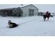 Snowy scene shows a person on a horse pulling a on a sled with a white barn and trailer in the background at 32350 E 137Th Way, Brighton, CO 80603