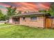 Charming brick home featuring a manicured lawn, attached garage, and privacy fence under a colorful sky at 7995 Robin Ln, Denver, CO 80221