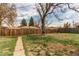Expansive backyard with a weathered wooden fence, mature trees, and a concrete walkway leading through the grass at 9280 Russell Way, Thornton, CO 80229