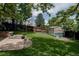 Backyard showcasing a grassy lawn, stone steps, and a storage shed surrounded by mature trees and fencing at 12631 W Dakota Dr, Lakewood, CO 80228