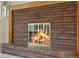 Close-up of a brick fireplace with a decorative wood mantel and a lit fire behind glass doors at 7346 S Platte Canyon Dr, Littleton, CO 80128