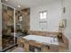 Modern bathroom featuring earth-toned stone tiles, glass shower, and soaking tub beneath double windows at 8044 E 24Th Ave, Denver, CO 80238