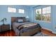 Blue bedroom with hardwood floors, a cozy bed, three large windows, and stylish decor at 8044 E 24Th Ave, Denver, CO 80238