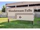 Exterior shot of the Woodstream Falls community sign with directional arrow, set against green grass at 9995 E Harvard Ave # 221, Denver, CO 80231