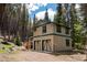 Two-story home exterior with two-car garage is nestled among pine trees and a gravel driveway at 446 Blue River Rd, Breckenridge, CO 80424