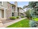 Townhouse with stone accents, green lawn, and mature evergreens creating an inviting entrance at 10311 E Evans Ave # 132, Aurora, CO 80247