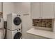 Bright laundry room with side-by-side machines, folding counter, mosaic backsplash and upper cabinets at 5677 S Park Pl # C111, Englewood, CO 80111