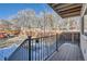 Backyard view from porch, showcasing a wooden deck, black metal railing, and fenced yard surrounded by mature trees at 6021 Yarrow St # B13, Arvada, CO 80004