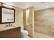 Bathroom with tan stone tile, a large mirror, and a shower featuring a transom window at 7895 W 67Th Ave, Arvada, CO 80004