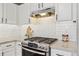 Close up of a gas range and modern oven with a stainless steel hood, herringbone backsplash, and white countertops at 684 Poppy Pl, Highlands Ranch, CO 80129