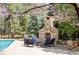 Outdoor stone fireplace and seating area near the pool, framed by mature trees and blossoming plants at 5550 Preserve Dr, Greenwood Village, CO 80121
