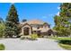Stunning home featuring manicured lawn, circular driveway, brick accents and mature trees under a blue sky at 7645 Fox Creek Trl, Franktown, CO 80116