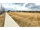 A vast field with a sidewalk alongside a road with neighborhood houses in the distance at 5686 Eagle River Pl, Brighton, CO 80601