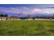 Open backyard with green grass, wooden fence and a set of chairs near a firepit under a colorful sky at 38 Morgan Cir, Erie, CO 80516