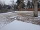 Expansive backyard featuring a wooden fence, mature trees, and a snow-dusted lawn for outdoor enjoyment at 2907 S Upham St, Denver, CO 80227