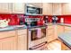 Close-up kitchen showcases stainless steel appliances, maple cabinets and a red backsplash at 13304 E Asbury Dr, Aurora, CO 80014