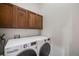 Functional laundry room with white washer and dryer, and wooden upper cabinets for storage at 2777 Ironton St, Denver, CO 80238