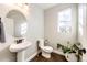 Well-lit half bathroom with pedestal sink, round mirror, wood-look floors, and decorative accents at 7150 E 121St Pl, Thornton, CO 80602