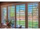 View of backyard through dining area shutters, featuring fenced yard, play structure, and well-maintained lawn at 14533 W 69Th Pl, Arvada, CO 80004