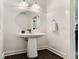Well-lit powder room with a pedestal sink, round mirror, and doorway view of the kitchen at 10479 E 25Th Dr, Aurora, CO 80010