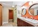 Bathroom featuring double sinks with a round mirror and warm orange accent wall at 10601 E Crestline Ave, Englewood, CO 80111