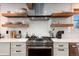 Modern kitchen with stainless steel range, white cabinets, and floating wood shelves at 6361 S Spotswood Cir, Littleton, CO 80120