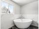 A modern, white, standalone tub sits beside a bright window with marble tile backdrop at 5153 Tucson Way, Denver, CO 80239