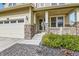 Charming front porch with stone pillars, a white railing, and lush landscaping. Two-car garage on the left at 14067 Hudson St, Thornton, CO 80602