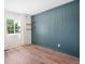 A bedroom with teal board and batten accent wall, a window with bright natural light and wood laminate flooring at 6318 Newton Ct, Arvada, CO 80003