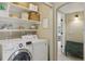 A bright laundry room with white washer and dryer and shelving that leads into the hallway at 10570 Humboldt Peak Way, Parker, CO 80138