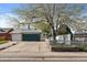 View of the garage with a large tree in the yard, a spacious driveway and white picket fence at 18902 E 17Th Ave, Aurora, CO 80011