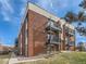 Exterior view of a red brick apartment building with black metal balconies and well-maintained lawn and landscaping at 5995 W Hampden Ave # 23, Denver, CO 80227