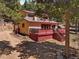 View of the exterior with a large deck, beige siding, and red trim surrounded by trees at 10852 Conifer Mountain Rd, Conifer, CO 80433
