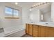 Bright bathroom featuring a soaking tub, window, and double sink vanity with wooden cabinets at 2062 S Xenia Way, Denver, CO 80231