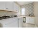 Well-lit laundry room with patterned accent wall, white cabinets, and modern washer and dryer at 23230 E Rockinghorse Pkwy, Aurora, CO 80016