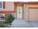 Close-up of a home's front entry with brick accents, a storm door, and colorful flowering bushes at 11112 Dahlia Way, Thornton, CO 80233