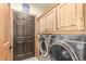Laundry room with wood cabinets, modern washer and dryer units, and a door at 46303 E 106Th Ave, Bennett, CO 80102