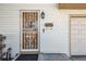 Close-up of front door with decorative metal security screen and white siding, complemented by classic outdoor lighting at 7815 Conifer Rd, Denver, CO 80221