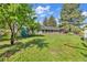 A view of the backyard showcasing the lush grass and the exterior of the charming home, accented by mature trees and a white fence at 1830 Zang St, Golden, CO 80401