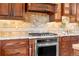 Close-up of the kitchen's stainless steel range and cooktop, complemented by tiled backsplash and wood cabinetry at 3418 Elk Ct, Broomfield, CO 80020