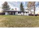 Large backyard with lush green grass, mature trees, a patio with chairs, and a white home at 3004 S Niagara Way, Denver, CO 80224